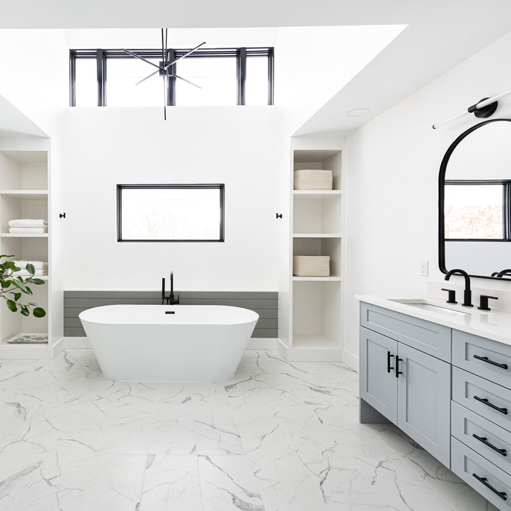 Expansive contemporary bathroom with large soaking tub, two story ceiling, white built-in cabinetry, blue double vanity and black fixtures