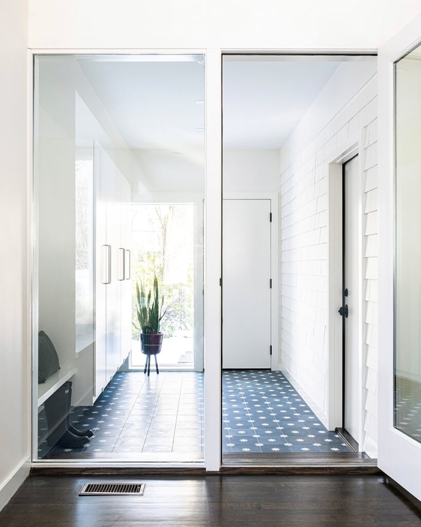 Modern mudroom with large glass window panes, white built-in cabinets, blue tile and dark hardwood steps