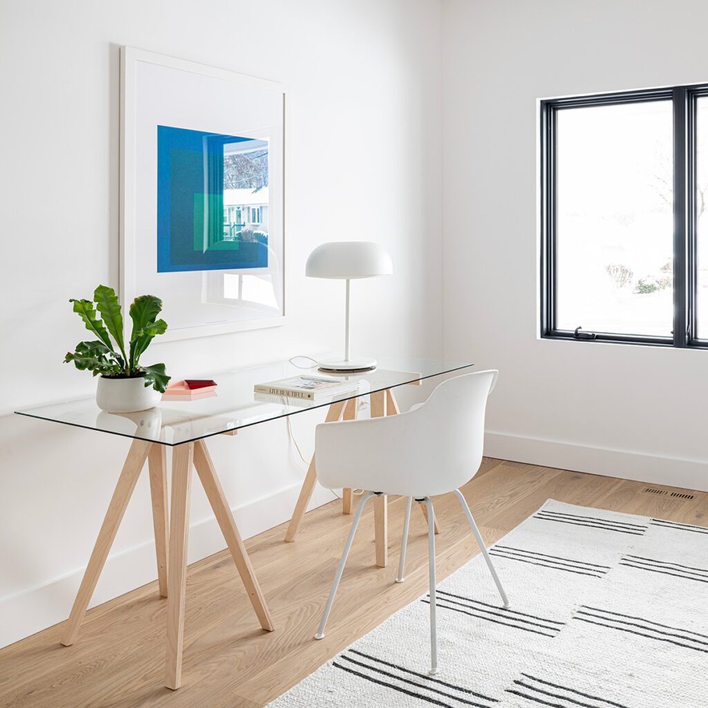 Minimalist glass desk with wooden legs, accompanied by a modern white chair, white table lamp, and potted plant