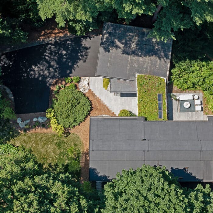 Aerial view of a mid-century modern house nestled among lush green trees, showcasing a live sedum roof, patio hardscaping and natural environment.